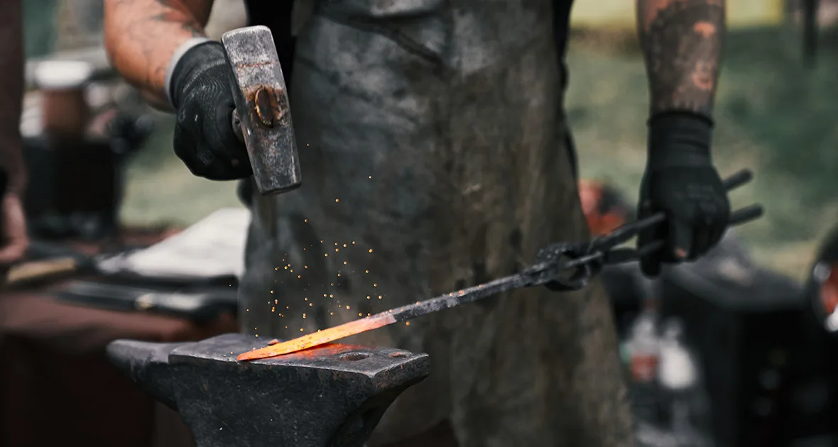 A blacksmith forging a blade on an anvil — sparks flying, metal glowing orange
